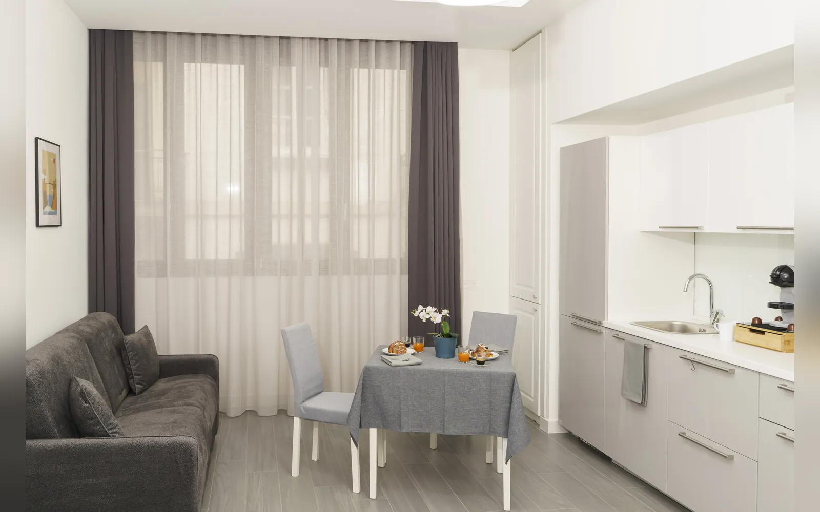La zona giorno con il divano, il tavolo e l’angolo cottura bianco